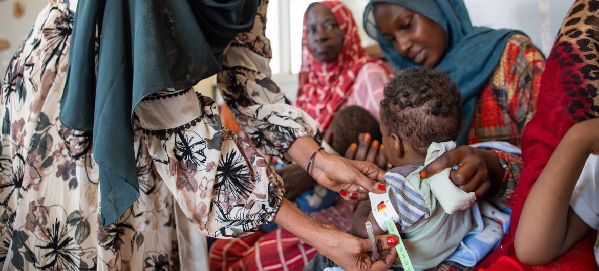 Um profissional de saúde mede uma criança em busca de sinais de desnutrição em Cartum, Sudão. Em todo o mundo, os conflitos e os choques relacionados com o clima estão a provocar o aumento da fome, deixando as famílias com dificuldades no acesso a alimentos, cuidados e estabilidade.