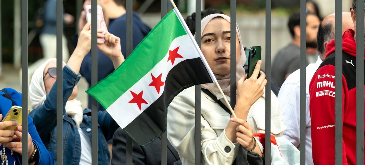 Uma mulher segura a nova bandeira da Síria em frente à sede da ONU em Nova York. (abril de 2025)