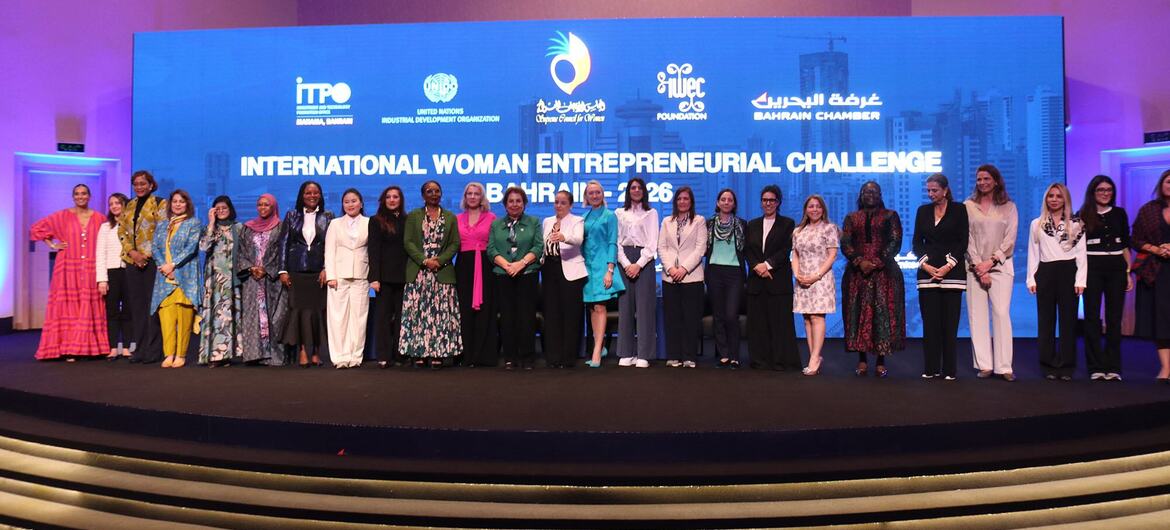 Um grupo de mulheres empreendedoras posa para uma foto no palco do International Woman Entrepreneurial Challenge 2026 em Manama, Bahrein, com os logotipos dos eventos exibidos em uma grande tela atrás delas.