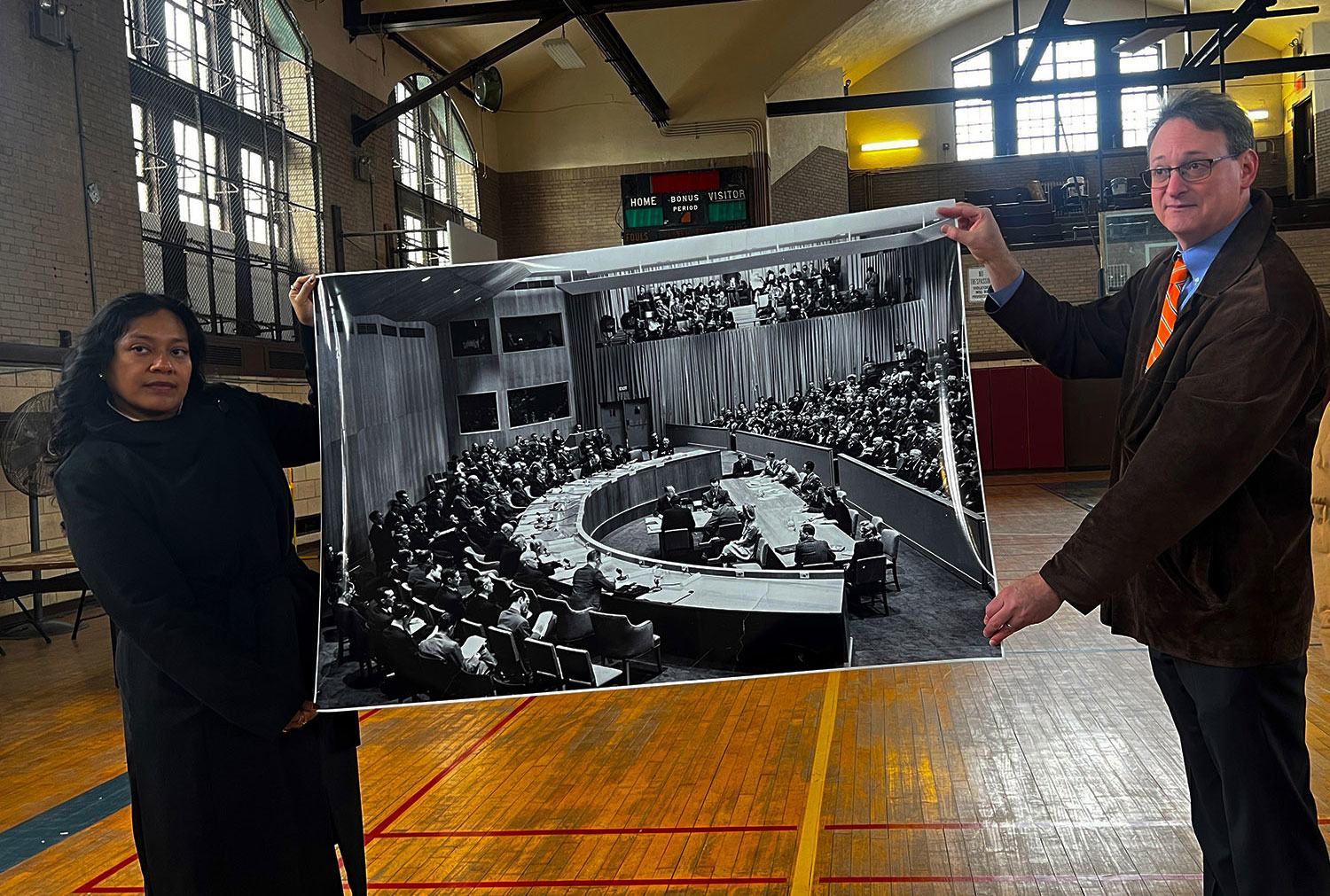 Dois atuais funcionários do Lehman College seguram uma fotografia do Conselho de Segurança da ONU de 1946, que já ocupou a quadra de basquete da faculdade.
