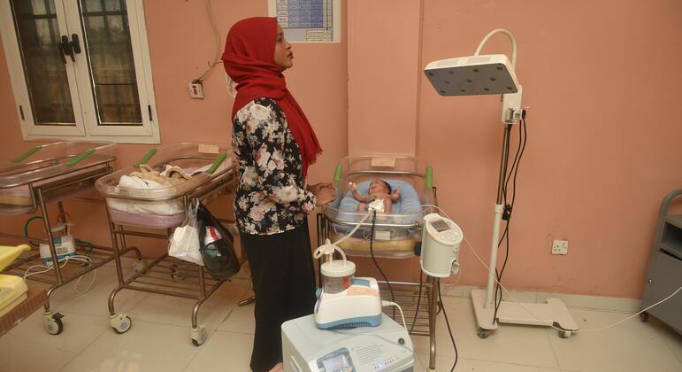 Uma parteira com um hijab vermelho monitora um bebê recém-nascido em uma incubadora no Hospital Maternidade El Obeid, no Sudão. O hospital abriu uma nova unidade neonatal em 2026 com apenas quatro leitos, destacando a necessidade urgente de ampliação da capacidade.