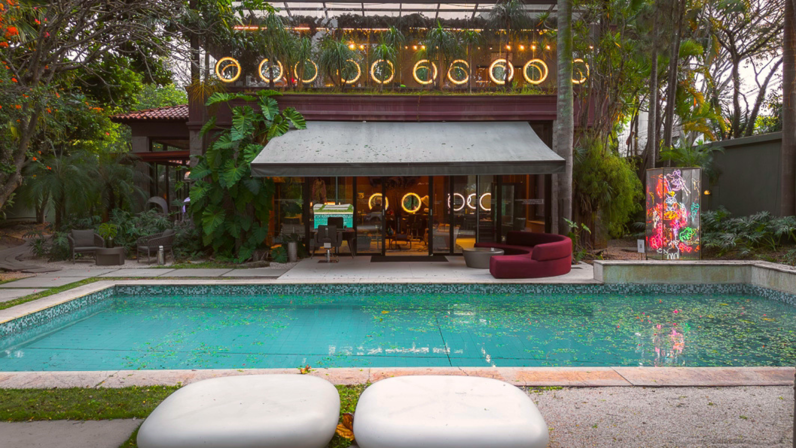 Fachada da Casa Conceito em São Paulo, com área externa integrada, piscina, paisagismo tropical e ambiente sofisticado iluminado.